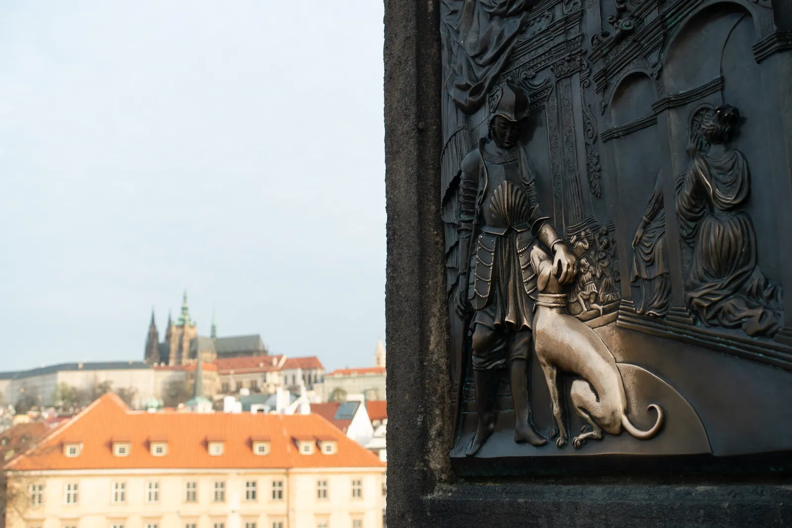 A bronze relief on a bridge parapet, a castle across the river beyond.