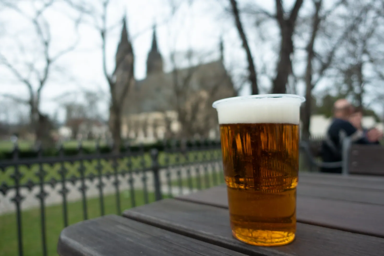 A glass of beer on a café table, gothic church spires behind bare trees.