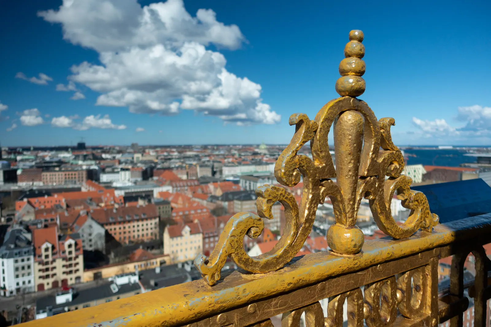 Red rooftops and harbour seen past a gilded railing high above the city.