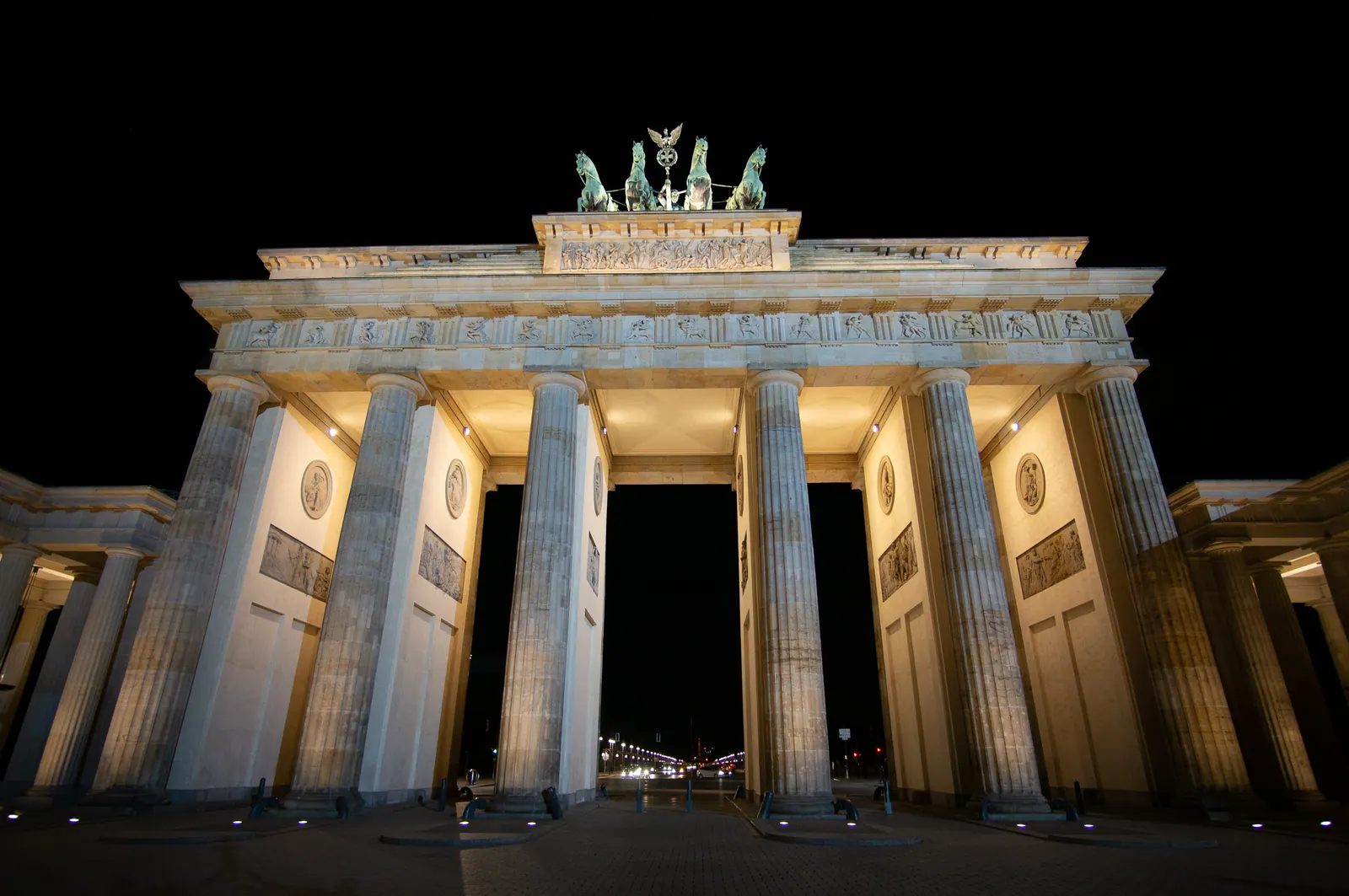 A floodlit neoclassical gate against a black night sky.