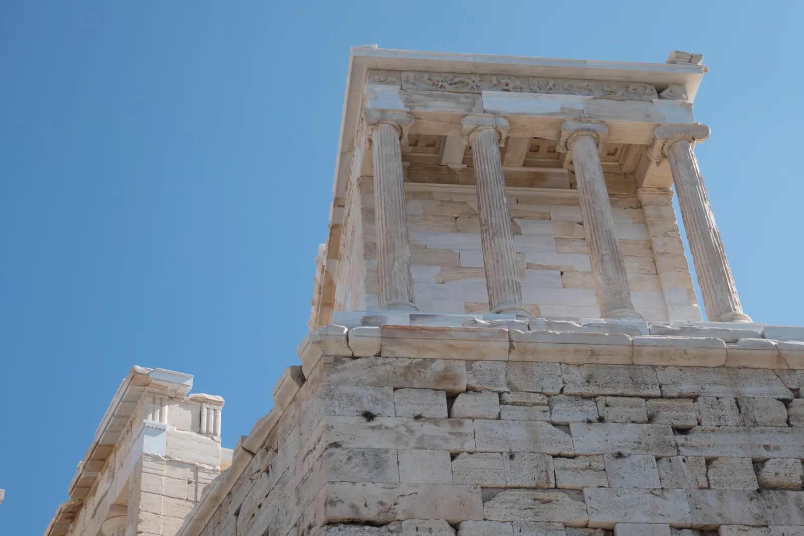 The corner of a marble temple seen from below against blue sky.