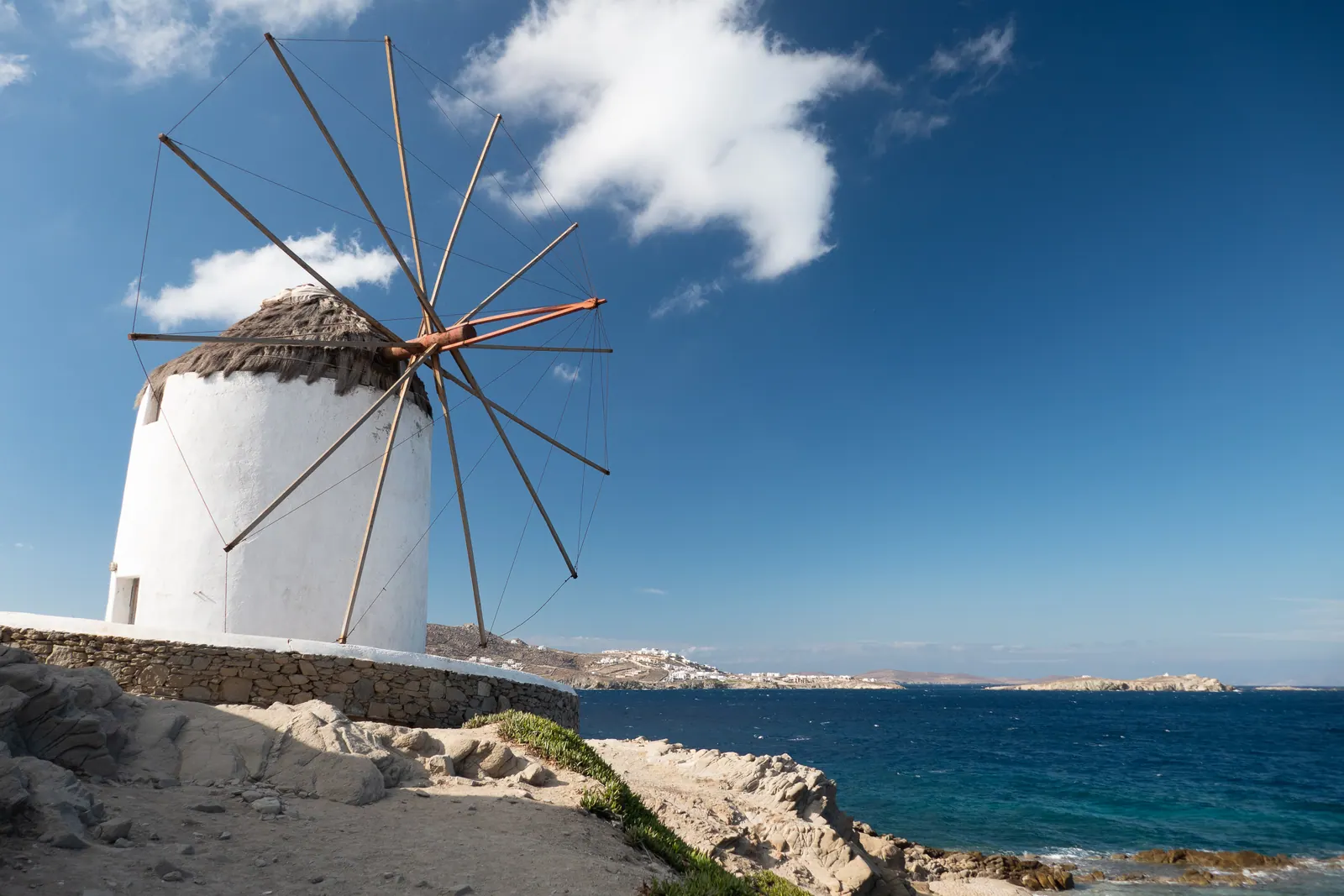 A white windmill with bare sail arms above the sea.