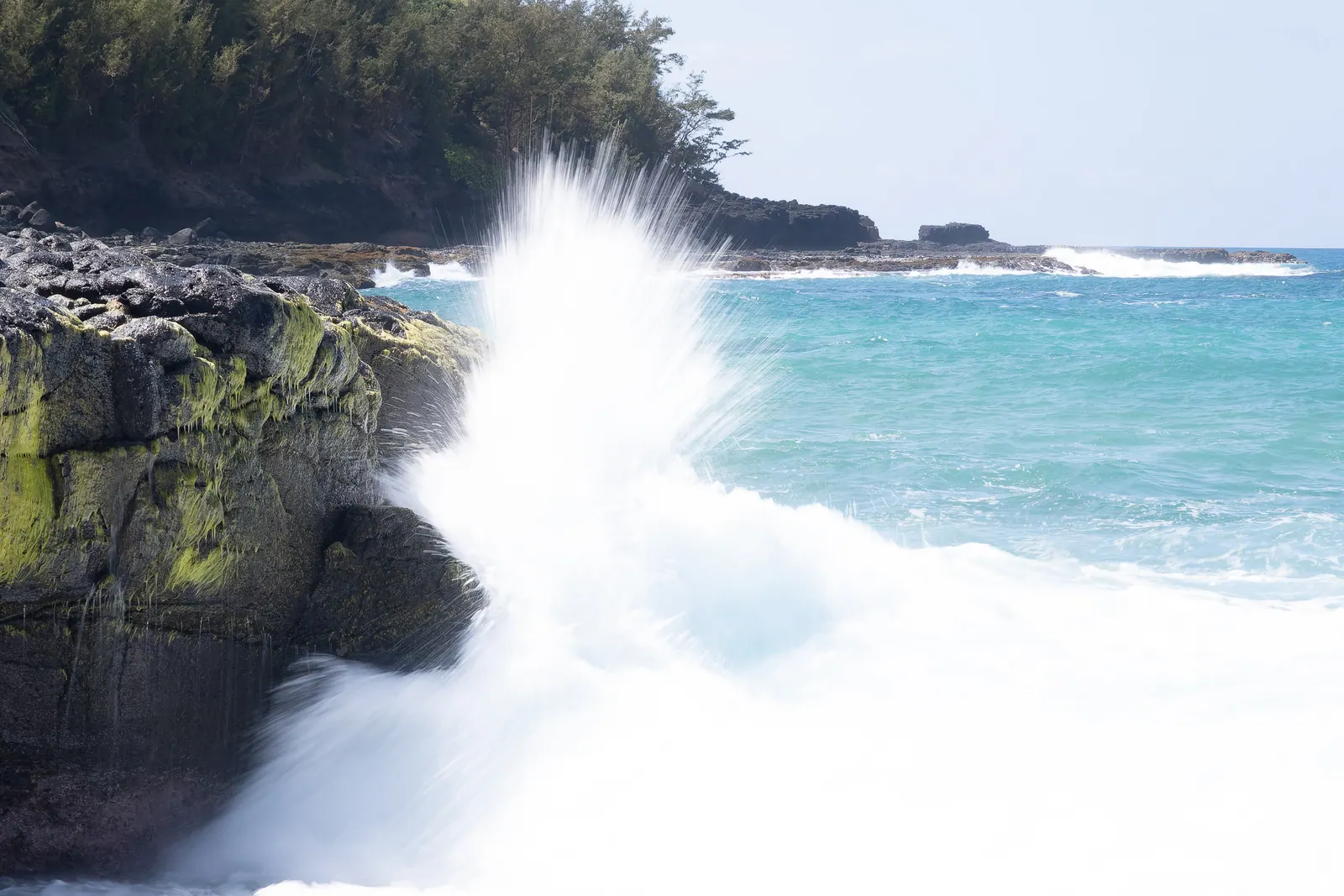 A wave exploding against black lava rocks.