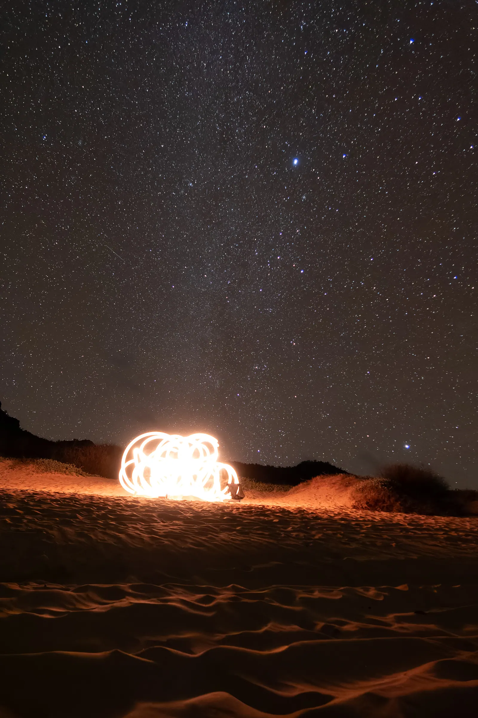 A burst of sparks lighting the sand under a starry night sky.