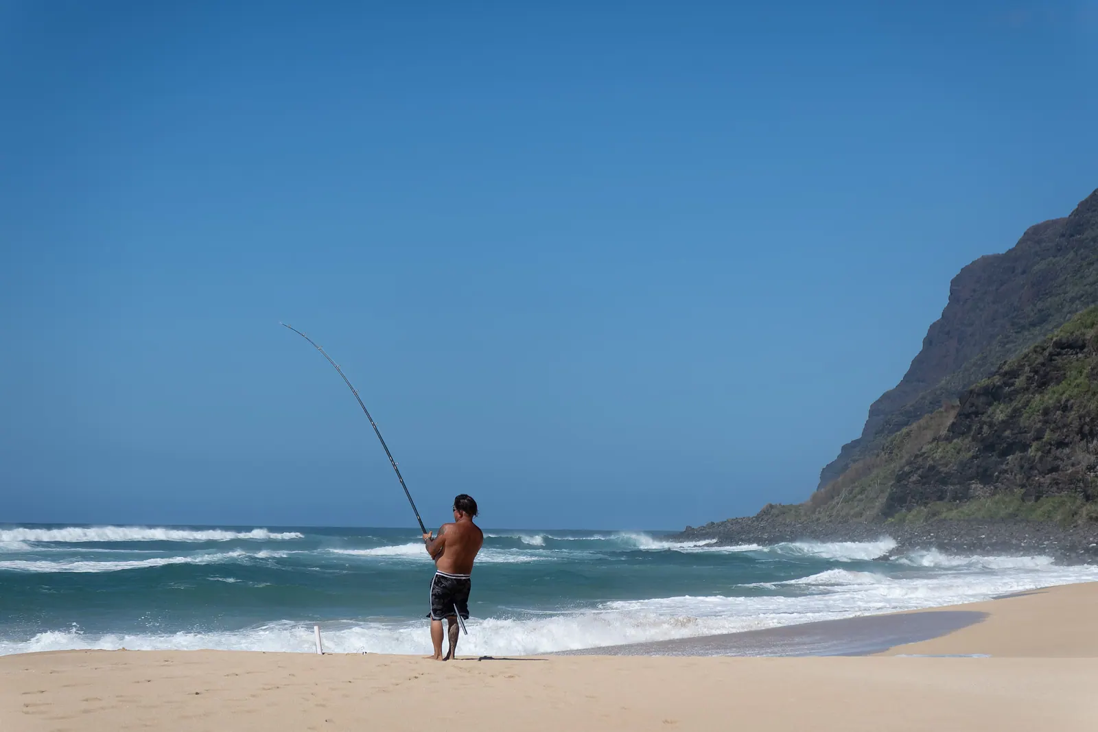 A person fishing from the beach, cliffs fading into haze behind.