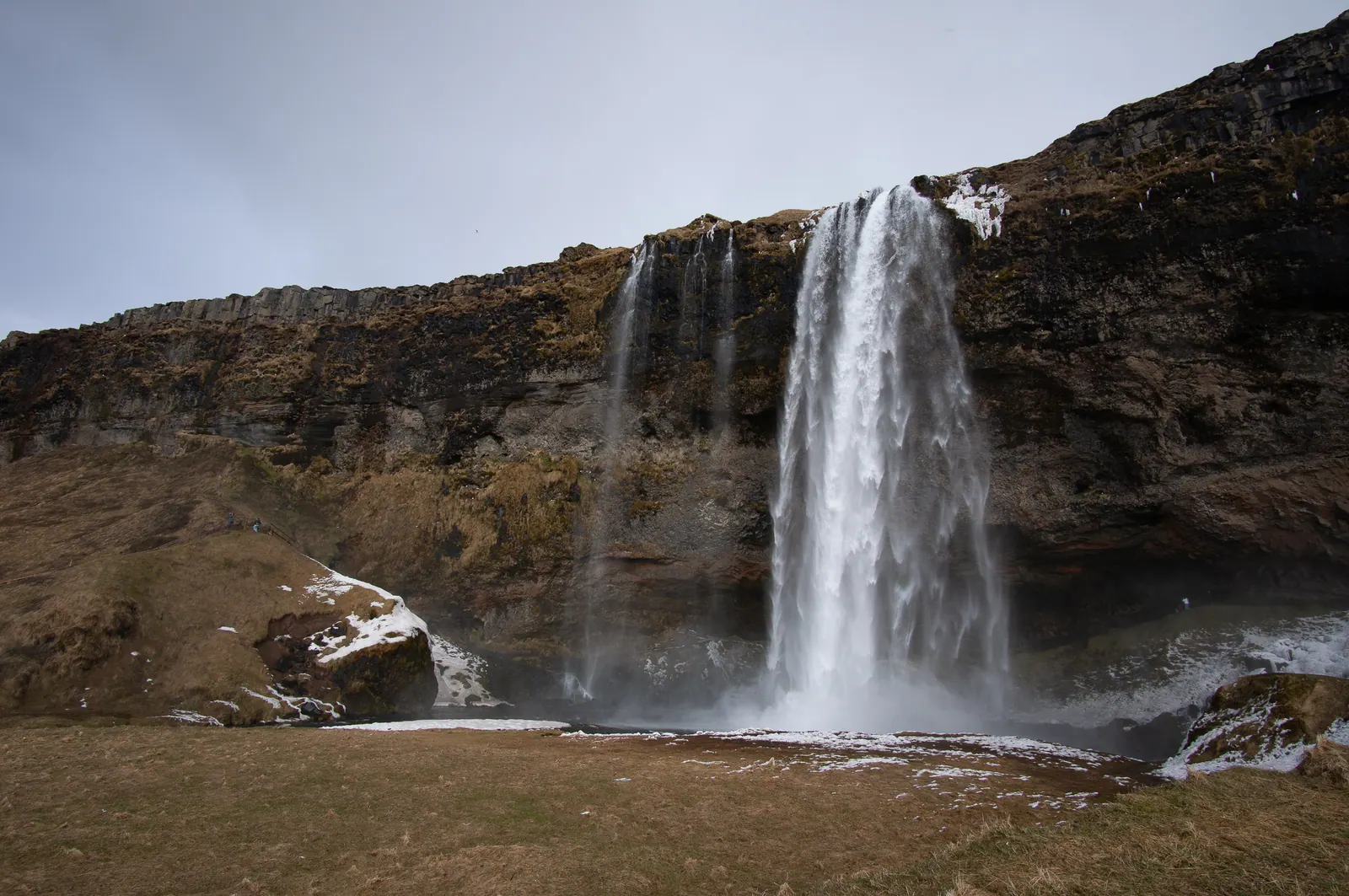 Waterfall falling from a mossy cliff onto a green plain.