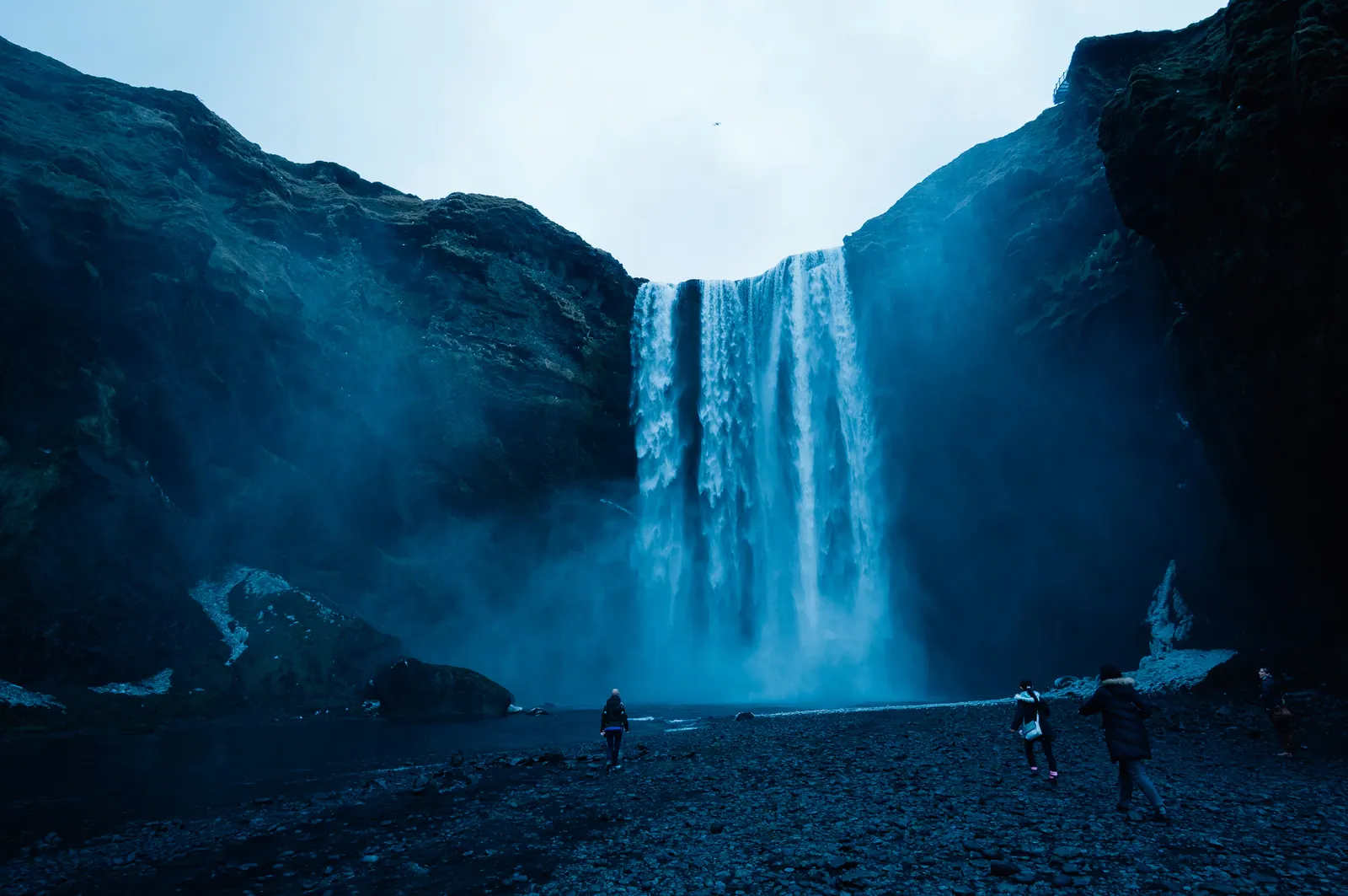 A broad waterfall in mist, small figures at its base.