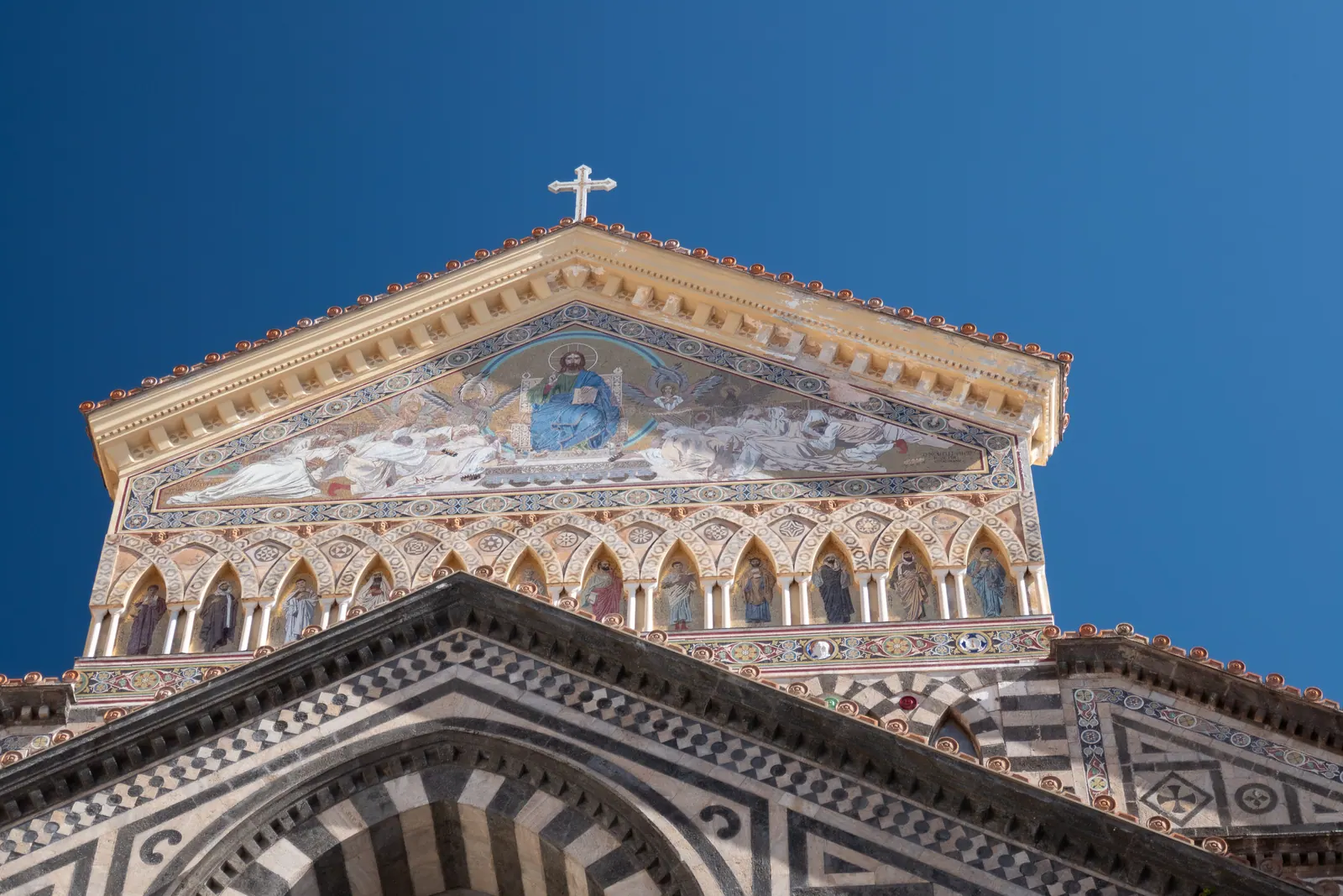 The striped facade and mosaic gable of a cathedral against blue sky.