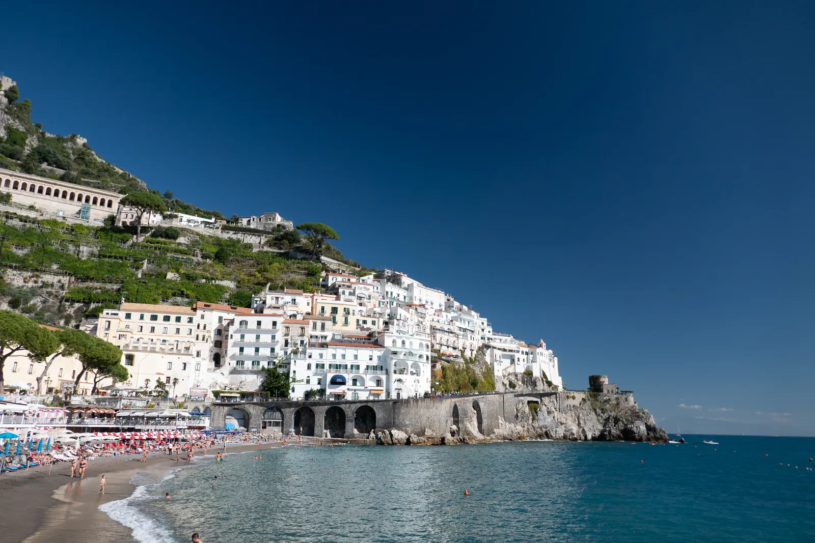 A town of white buildings stacked on a cliff above a beach.