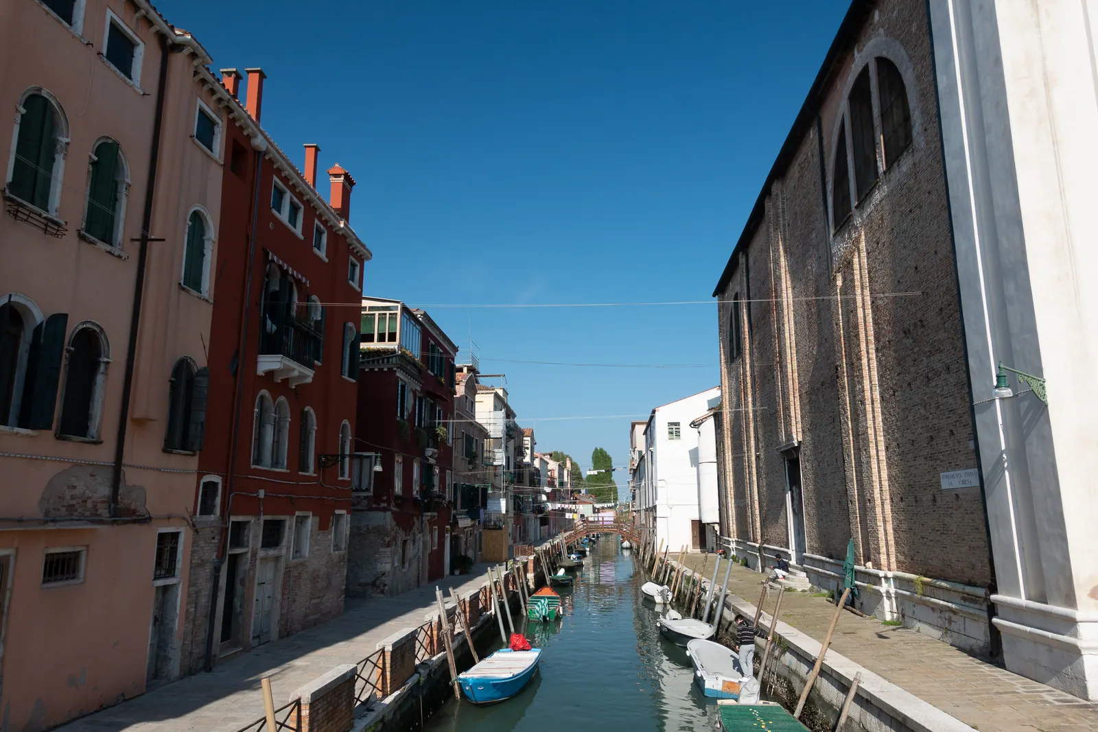 A narrow canal between brick buildings, boats moored along it.