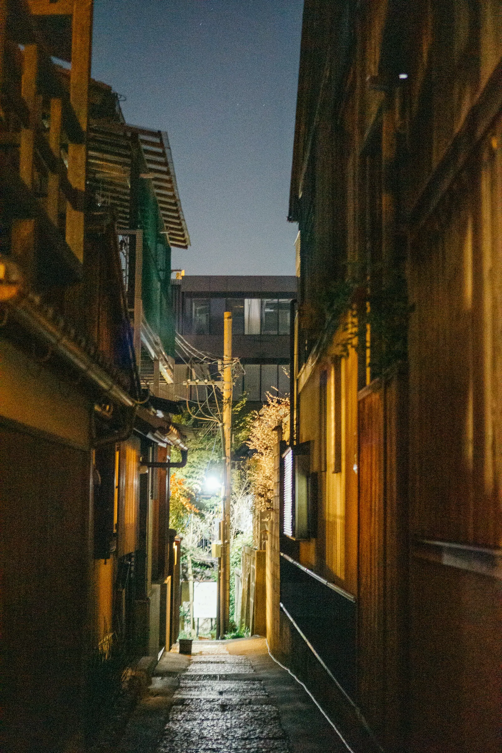 A narrow lane between dark wooden buildings, light at its end.