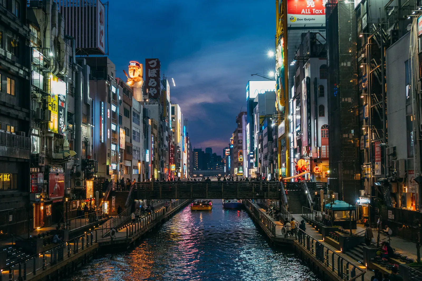 A canal lined with neon signs and buildings at dusk.