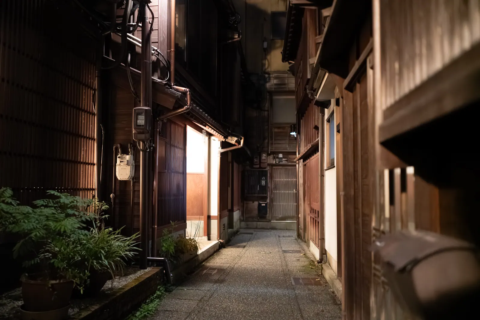 A narrow lane between weathered wooden houses and potted plants.