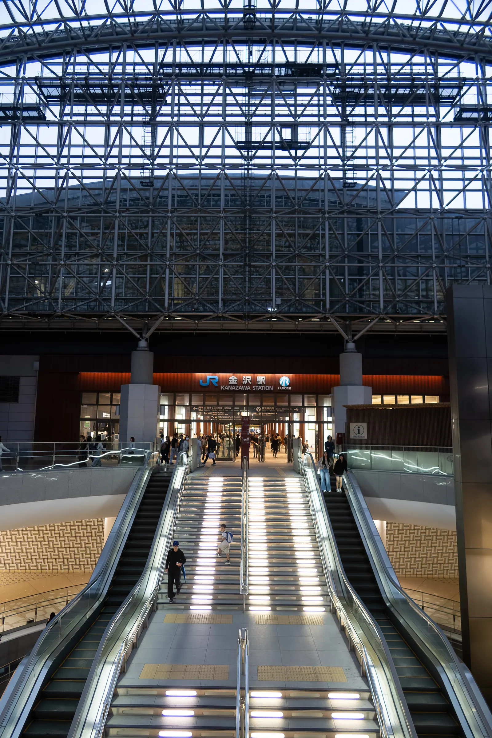 Escalators rising under the glass and steel roof of a station.