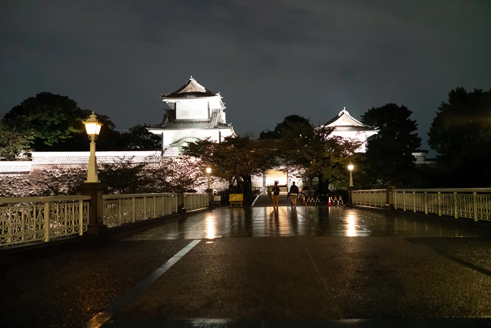 A white castle turret lit at night above wet paving.