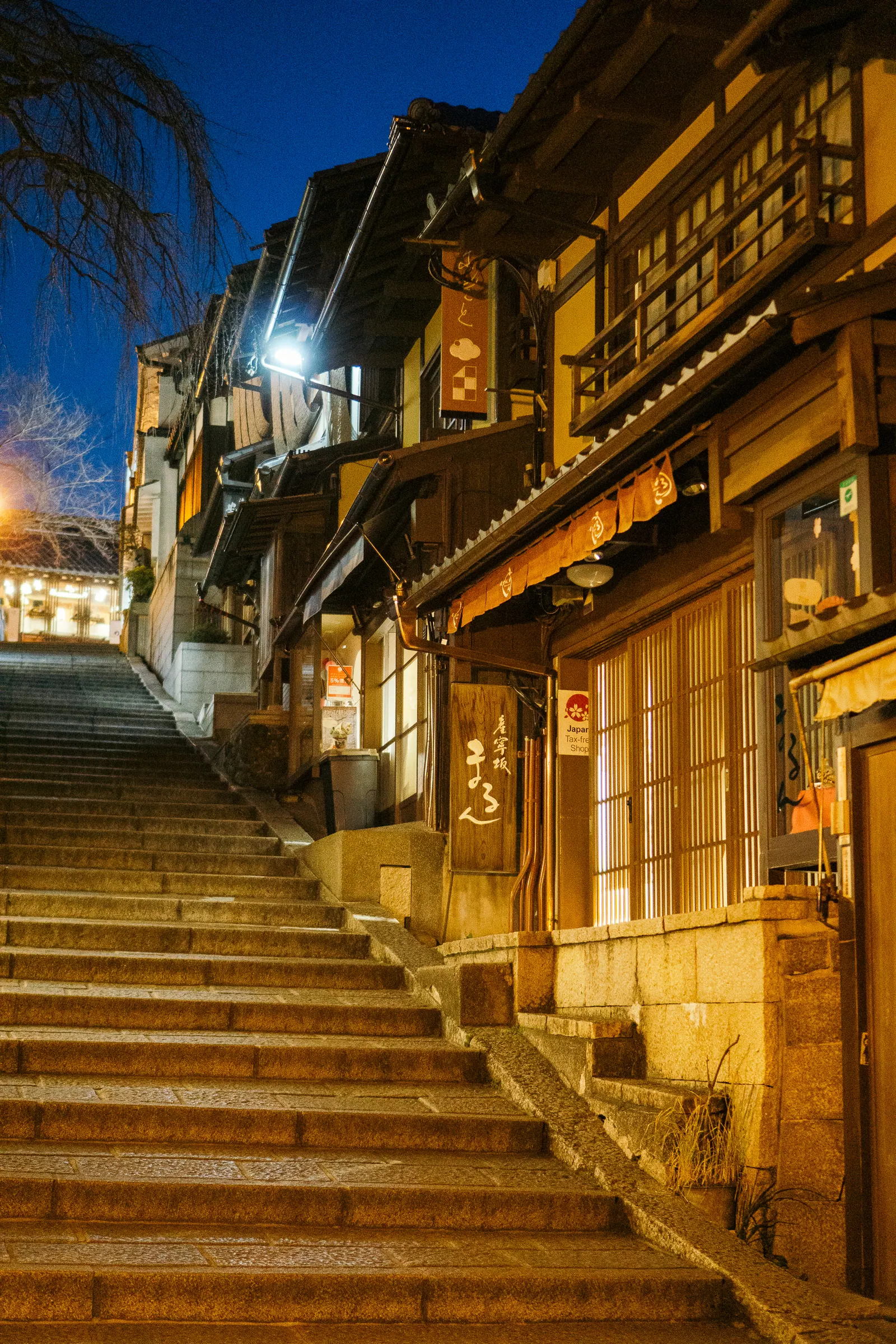 A lantern-lit stone stair between wooden houses at dusk.