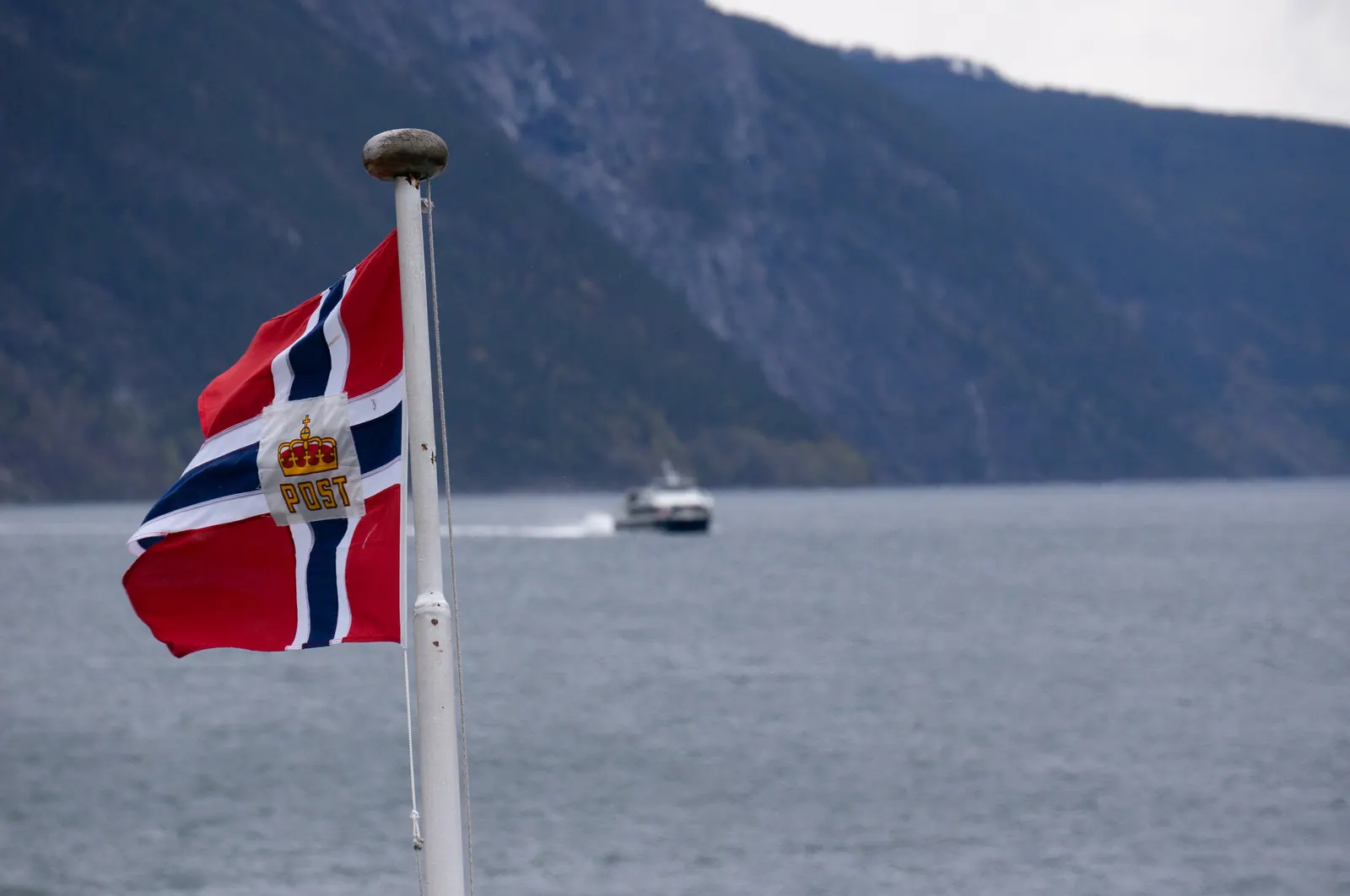 A Norwegian flag at the stern of a boat, fjord walls behind.