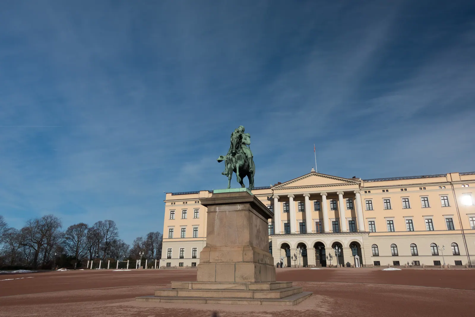 An equestrian statue in front of a pale palace under a deep blue sky.