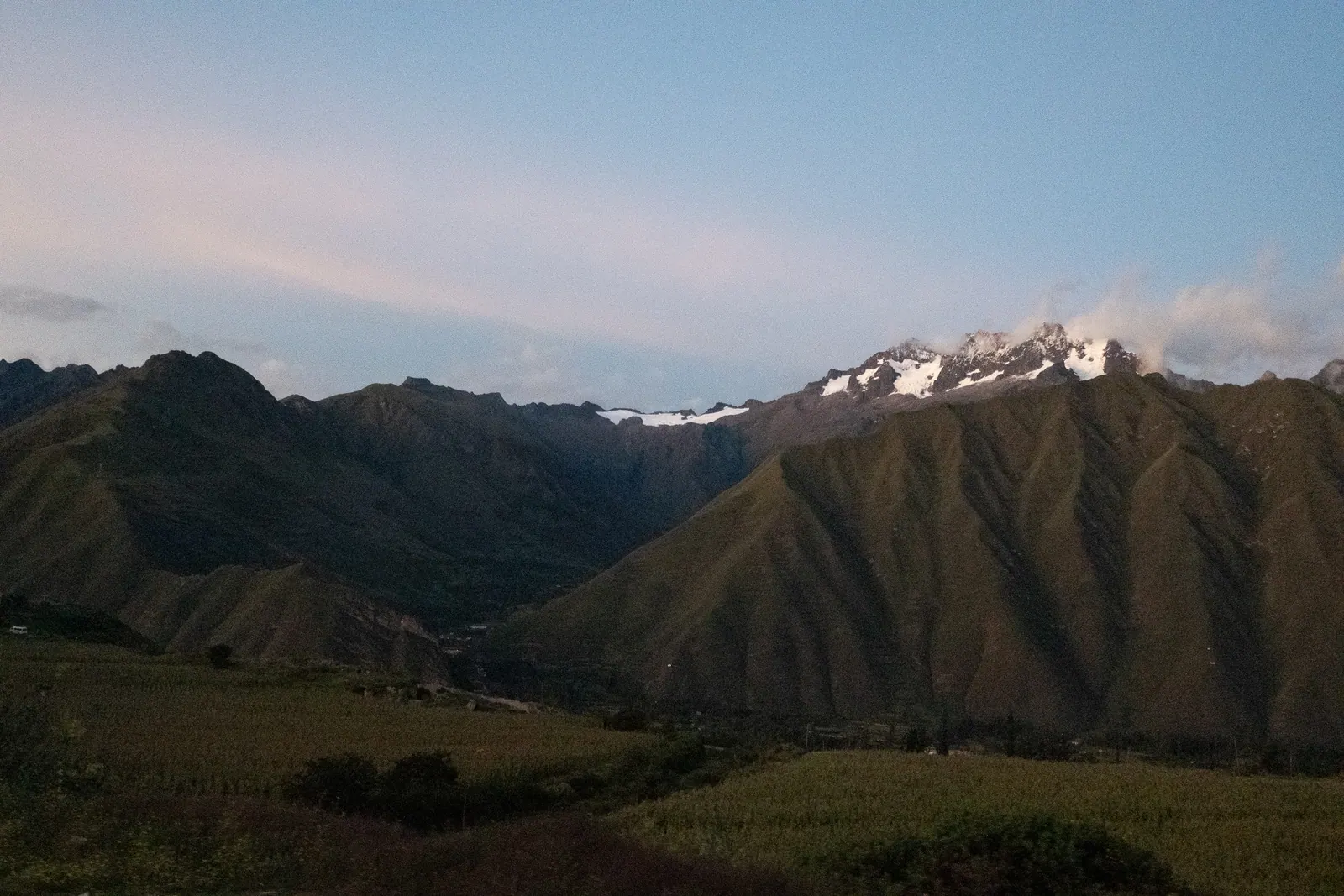 Green mountains with a snowy peak under an evening sky.