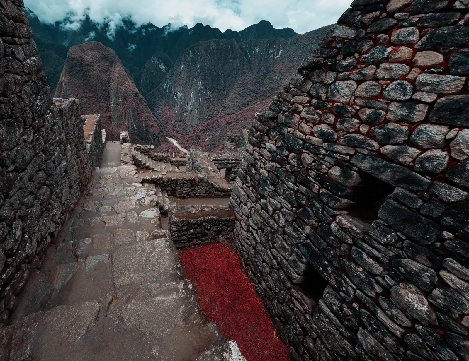Stone walls and a narrow stair in infrared, foliage rendered deep red, mountains in cloud behind.