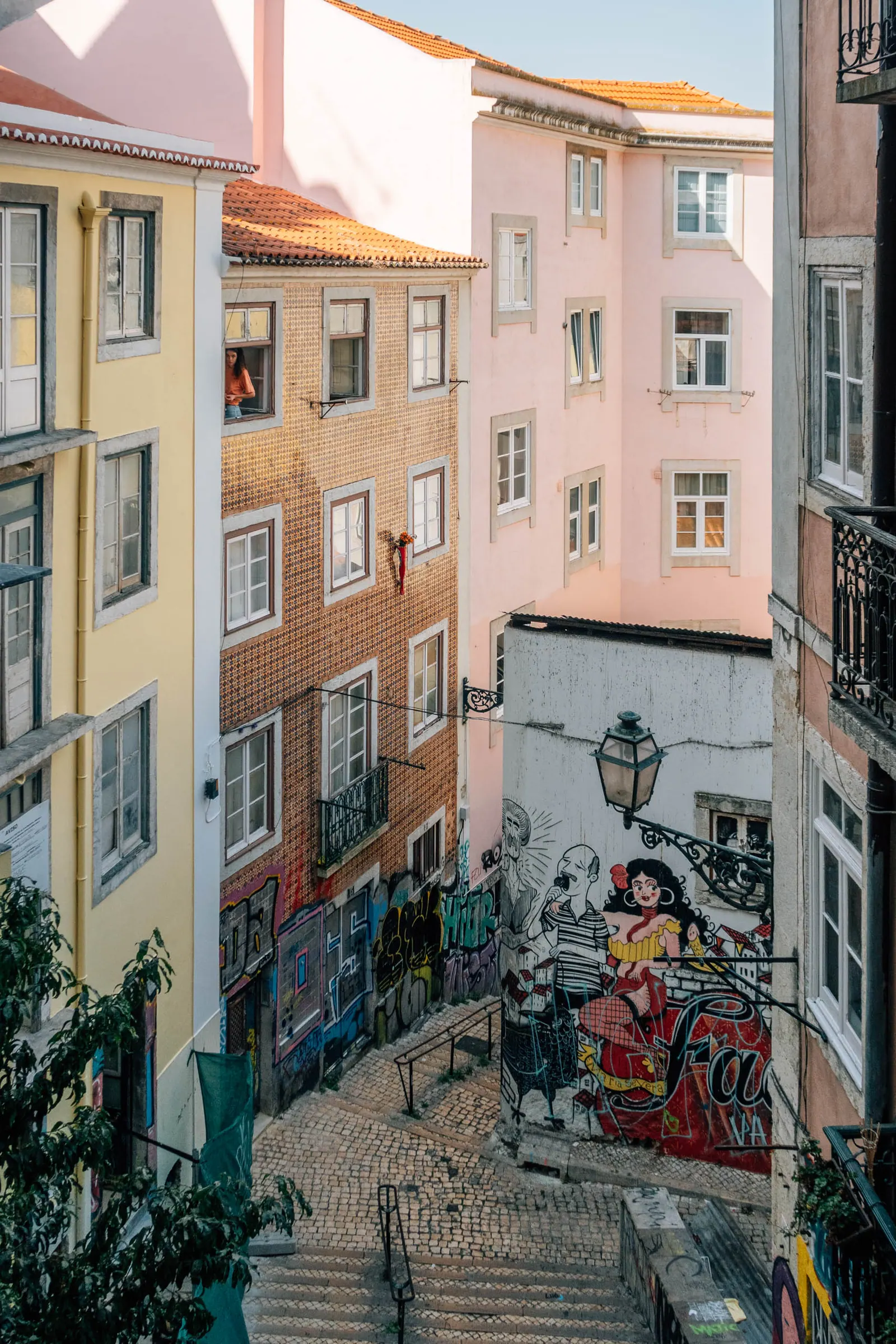 Looking down a stepped alley between pastel apartment buildings, murals covering the lower walls.