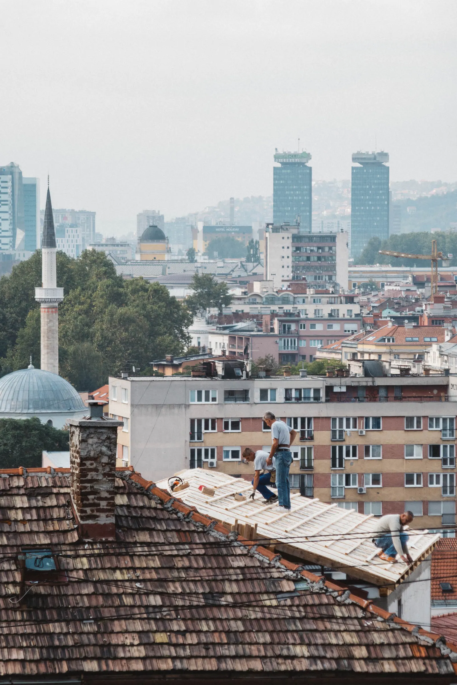 Workers repairing a tiled roof, a minaret and the city's high-rise towers behind.
