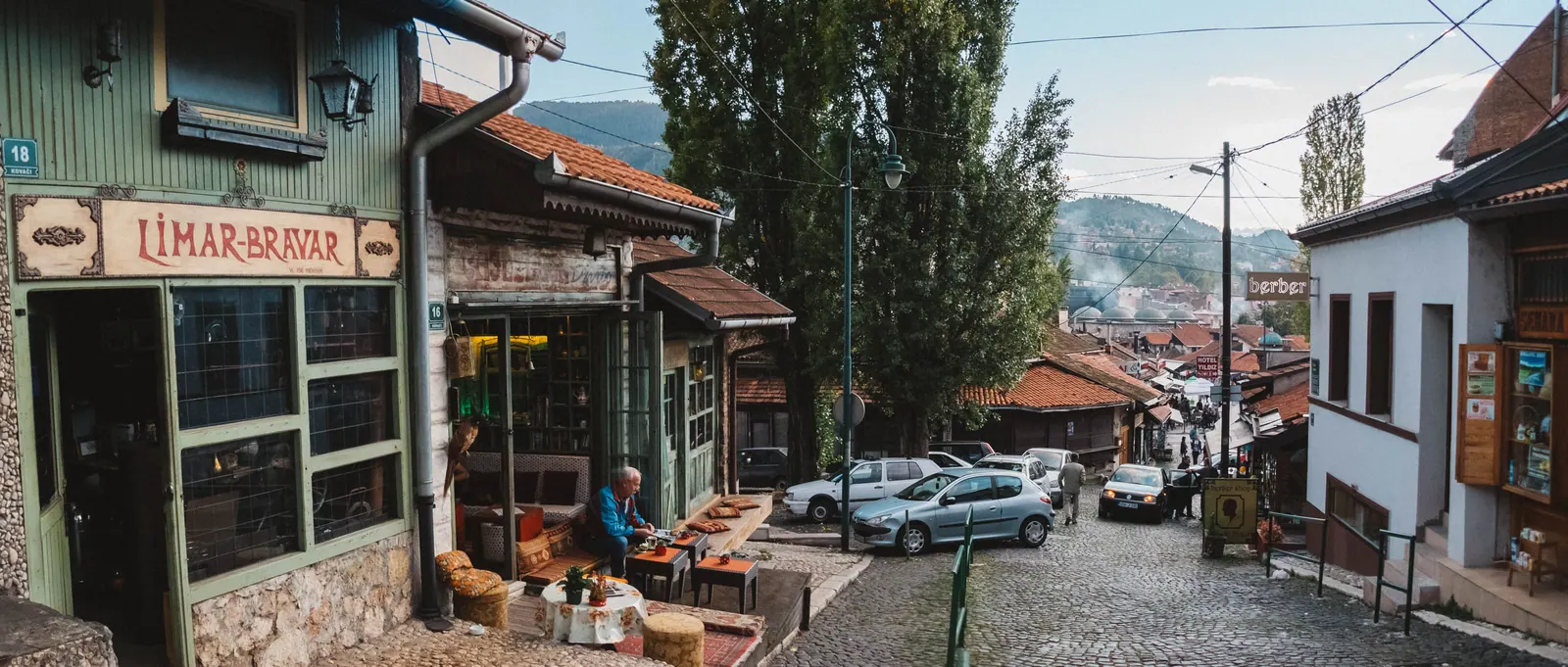 A steep cobbled street of old houses and a small shop, a man seated outside.