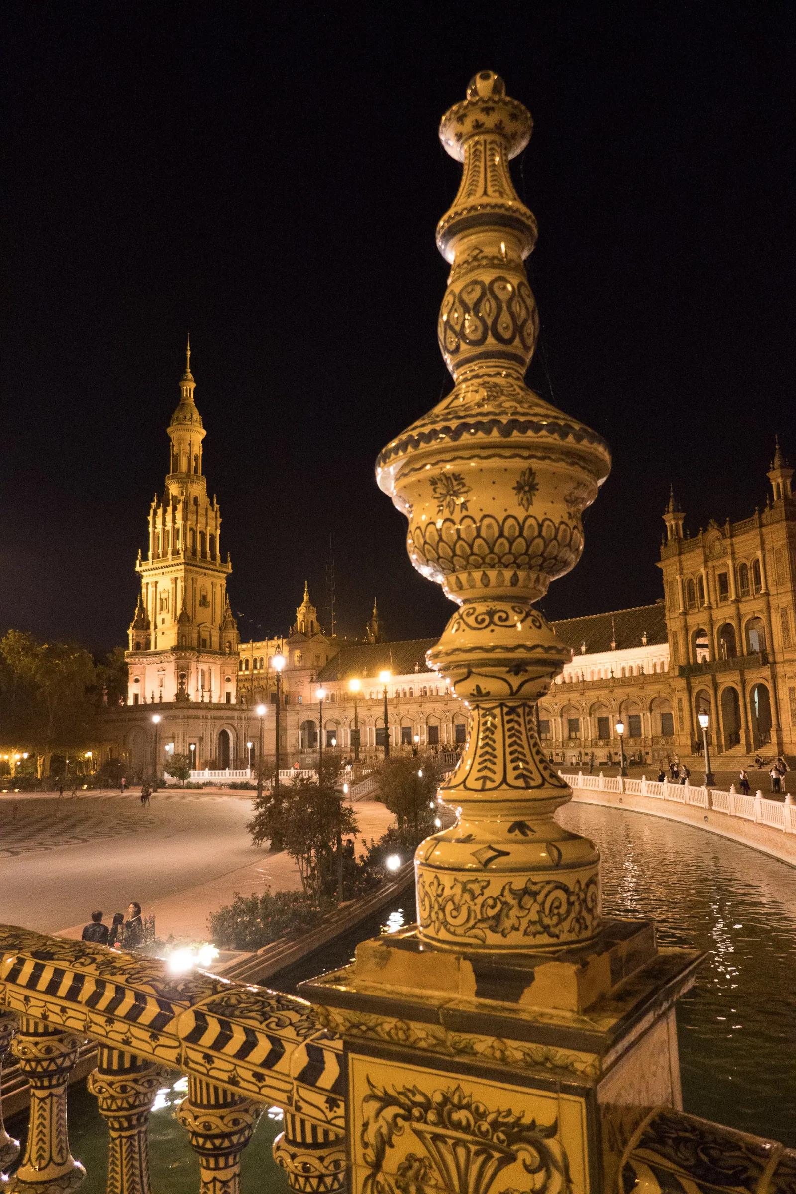 An ornate lamp post and a lit tower on a plaza at night.