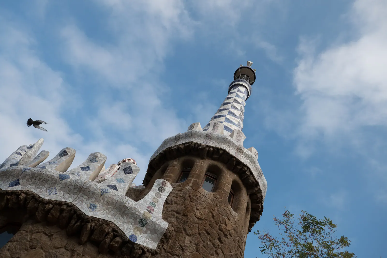 A mosaic-patterned tower top against clouds, a bird in flight.