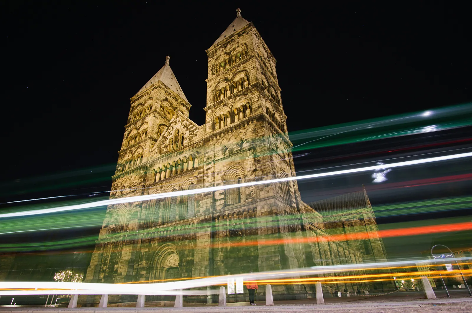 A twin-towered cathedral at night, streaked with passing light trails.