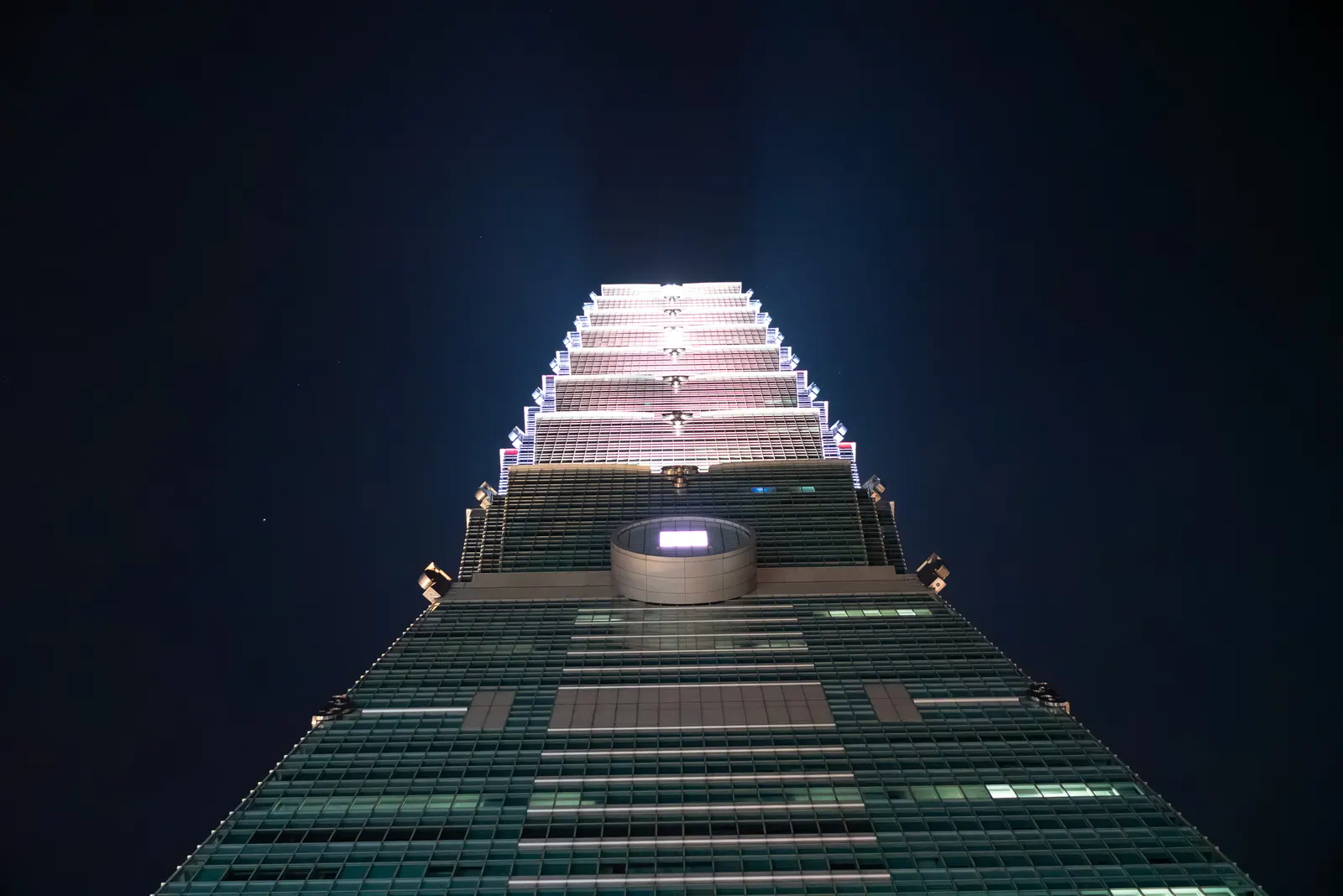 Looking up the lit tiers of a skyscraper against the night sky.