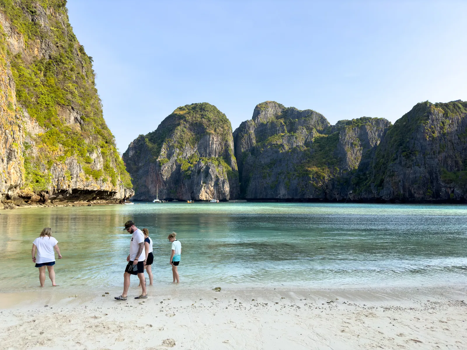 People on a white beach before sheer limestone cliffs.