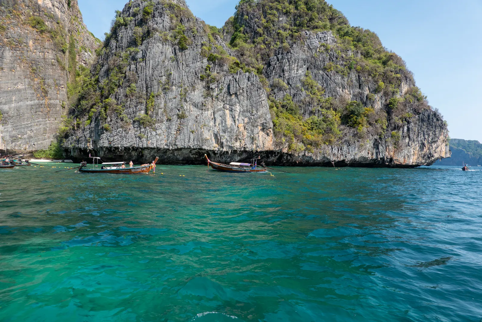 A limestone island rising from turquoise water, boats at its foot.