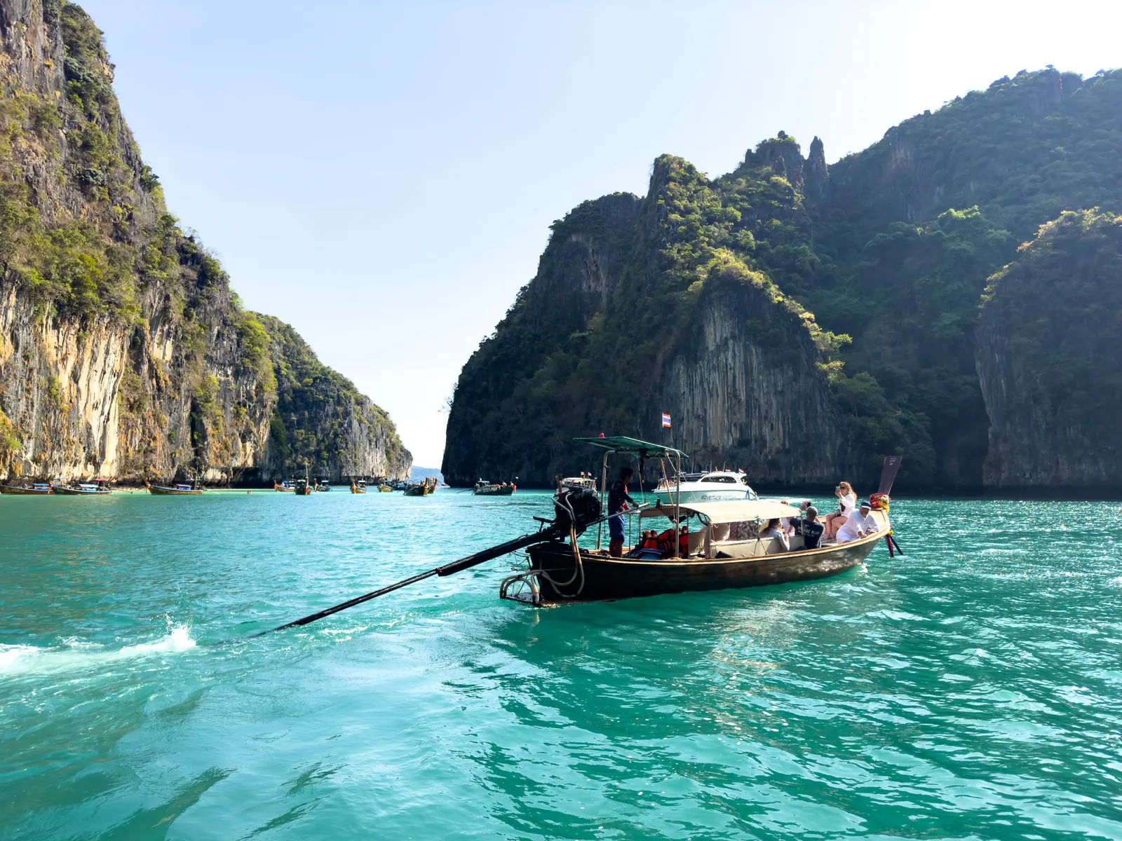 A longtail boat crossing a green bay between limestone cliffs.